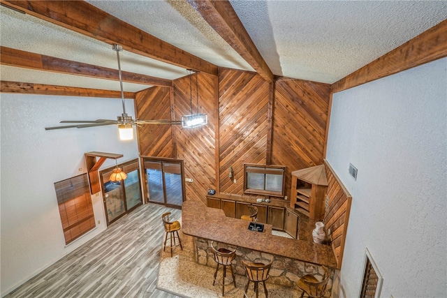 living room with wood walls, ceiling fan, light hardwood / wood-style floors, and beamed ceiling