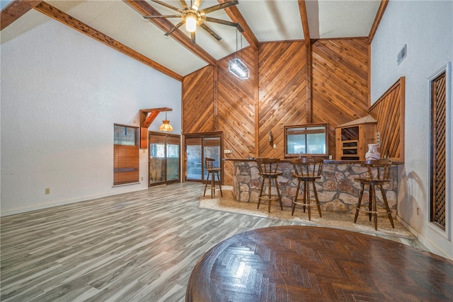 living room with wood walls, beam ceiling, high vaulted ceiling, and hardwood / wood-style floors