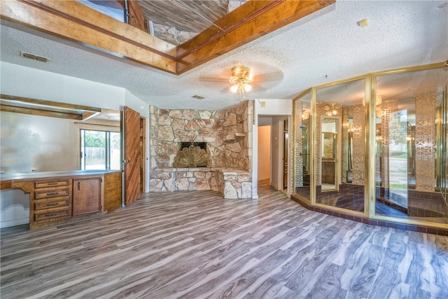 unfurnished living room featuring a stone fireplace, hardwood / wood-style floors, ceiling fan, and a textured ceiling