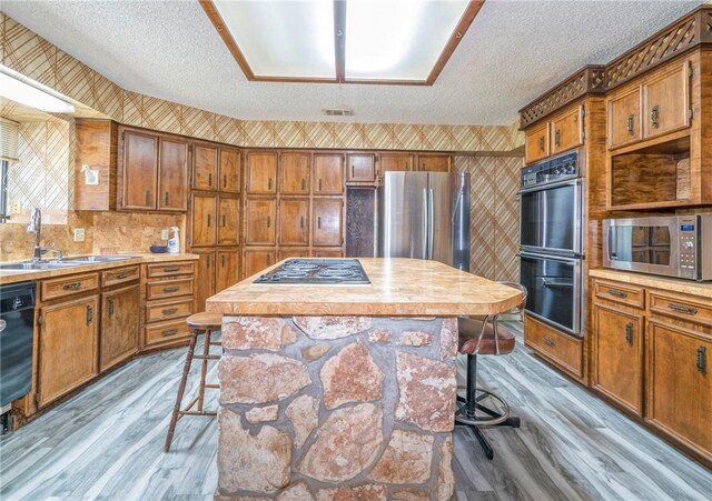 5490 County Road 73, Robstown, TX 78380 - kitchen featuring stainless steel appliances, wood finished floors, brown cabinetry, a textured ceiling, and wallpapered walls
