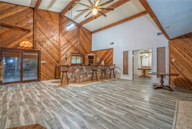 unfurnished living room with high vaulted ceiling, wood walls, hardwood / wood-style flooring, beamed ceiling, and ceiling fan with notable chandelier