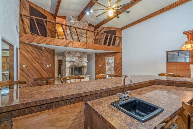 kitchen featuring wood walls, a stone fireplace, sink, and vaulted ceiling with beams