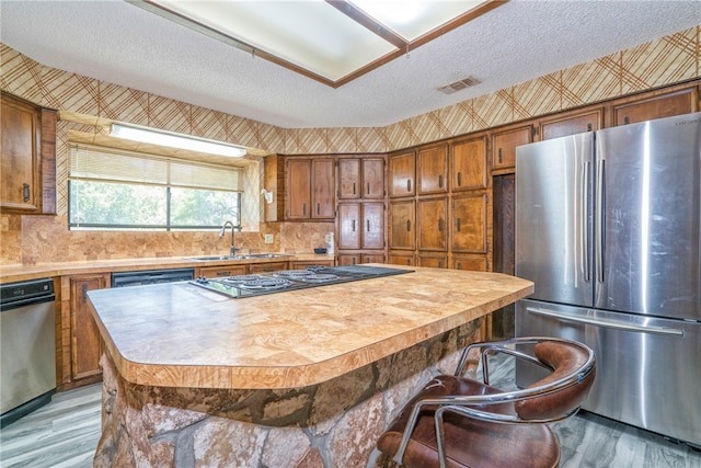 kitchen featuring a kitchen island, a textured ceiling, stainless steel refrigerator, sink, and light hardwood / wood-style flooring