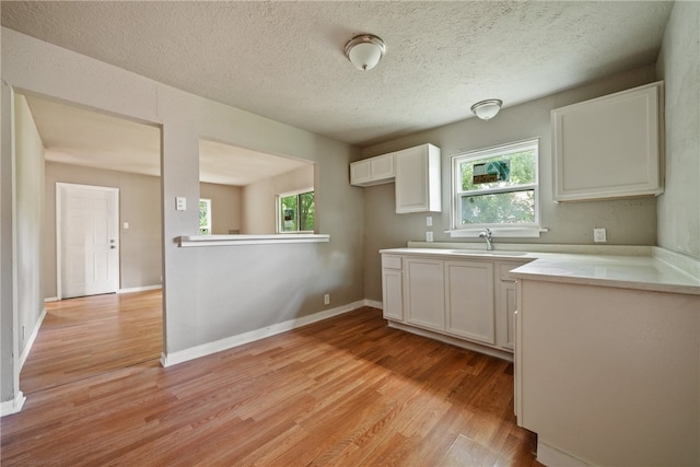 kitchen with a textured ceiling, white cabinetry, sink, and light wood-type flooring