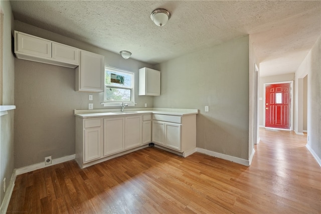 kitchen with white cabinetry, light hardwood / wood-style floors, a textured ceiling, and sink