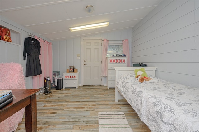 bedroom featuring light hardwood / wood-style floors, wooden walls, and vaulted ceiling