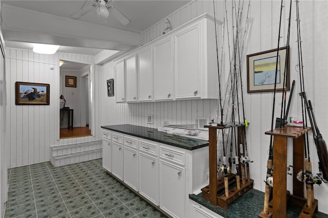 kitchen with wood walls, white cabinetry, and ceiling fan