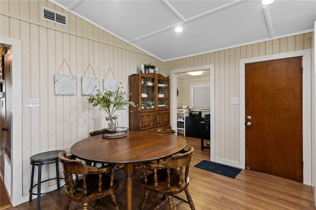 dining area featuring wood walls, lofted ceiling, hardwood / wood-style flooring, and ornamental molding