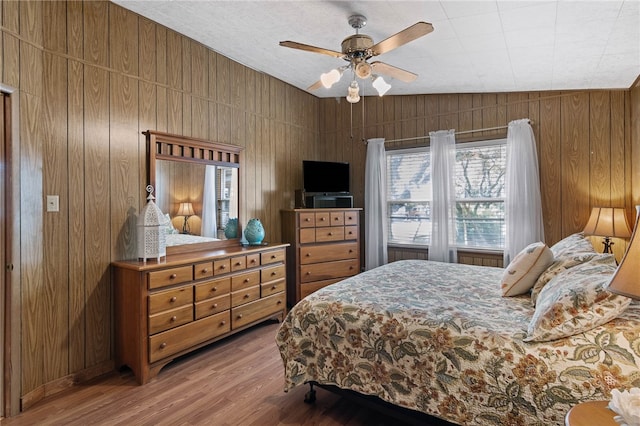 bedroom featuring hardwood / wood-style flooring, lofted ceiling, ceiling fan, and wood walls