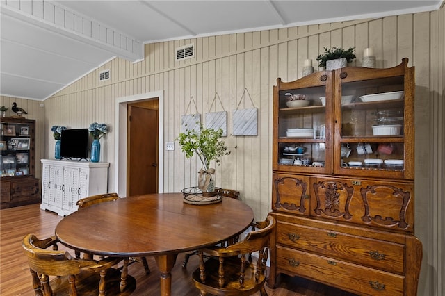 dining space featuring wood walls, hardwood / wood-style flooring, and vaulted ceiling with beams