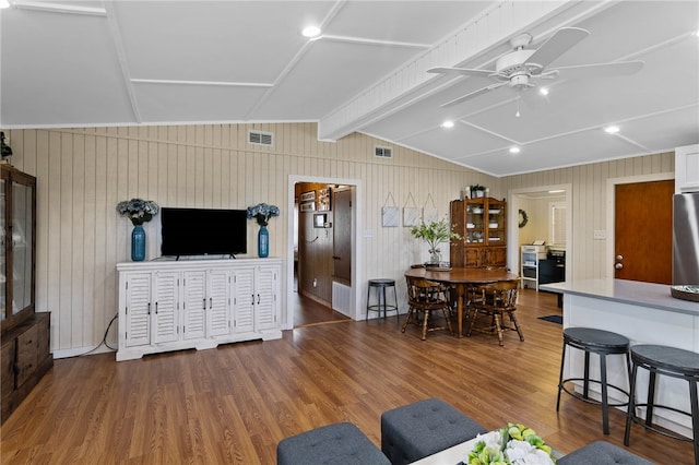 living room featuring hardwood / wood-style floors, ceiling fan, wood walls, and vaulted ceiling with beams