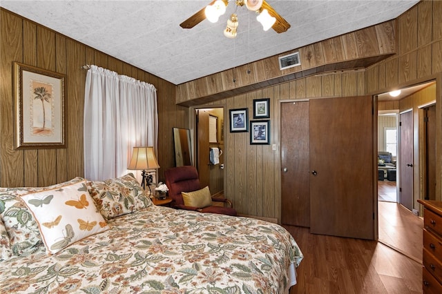 bedroom with wood walls, ceiling fan, a closet, and hardwood / wood-style floors