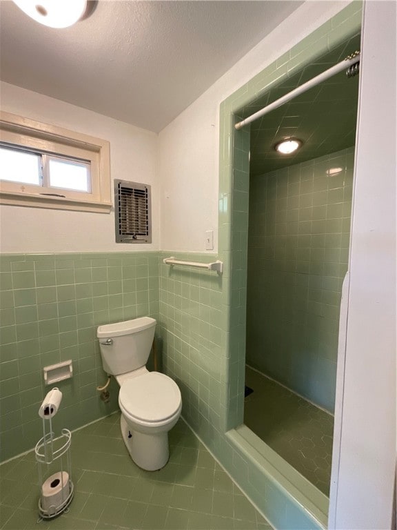 bathroom featuring tile walls, tile patterned floors, toilet, and tiled shower