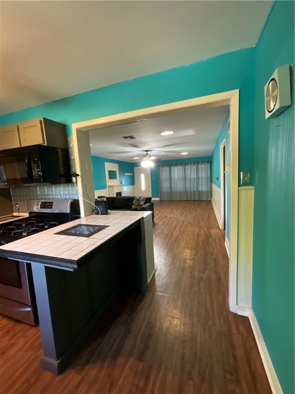 kitchen featuring dark hardwood / wood-style flooring, tile countertops, a breakfast bar area, stainless steel stove, and backsplash