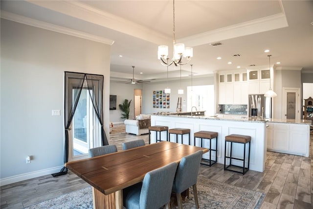 dining room featuring sink, a tray ceiling, ceiling fan with notable chandelier, and crown molding