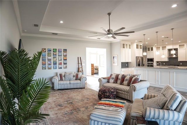 living room with ceiling fan, sink, ornamental molding, and a raised ceiling