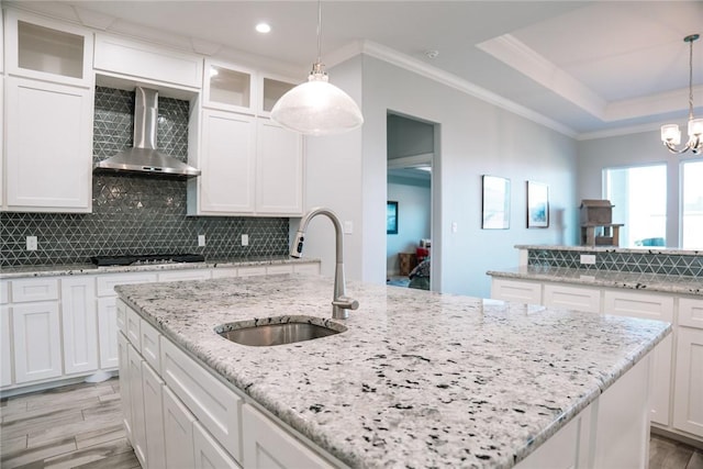 kitchen with decorative light fixtures, wall chimney exhaust hood, sink, and white cabinetry