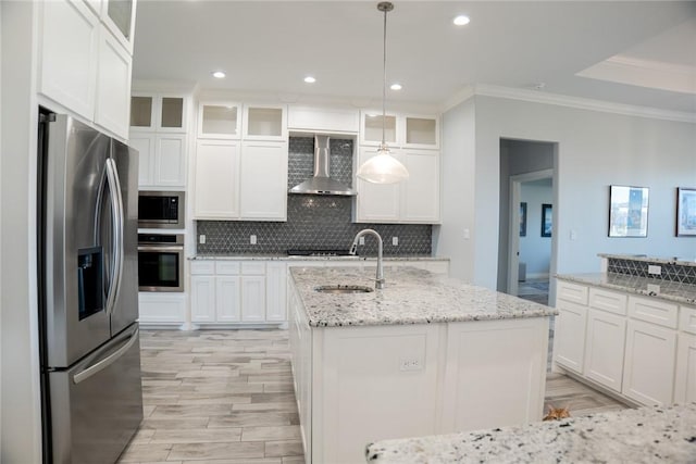 kitchen with an island with sink, stainless steel appliances, decorative light fixtures, wall chimney range hood, and sink