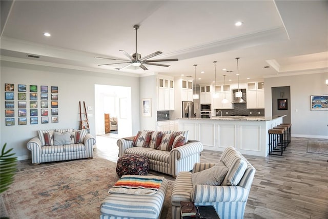 living room with a raised ceiling, wood-type flooring, ornamental molding, and ceiling fan