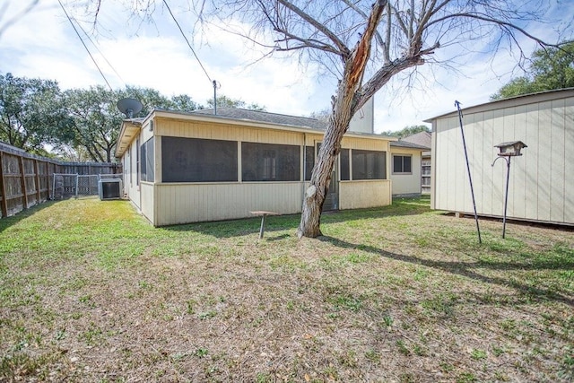 rear view of house with central air condition unit, a lawn, a sunroom, fence, and an outdoor structure