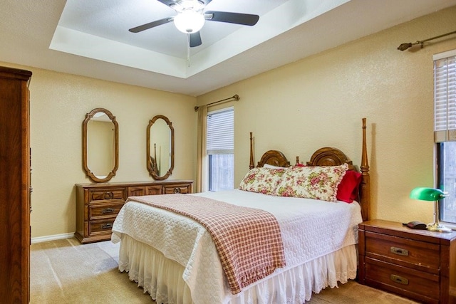 bedroom with multiple windows, a raised ceiling, and light colored carpet