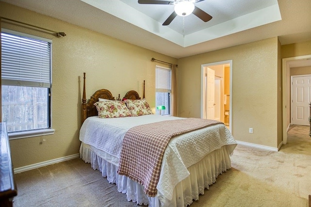 carpeted bedroom featuring a tray ceiling, a textured wall, baseboards, and ceiling fan