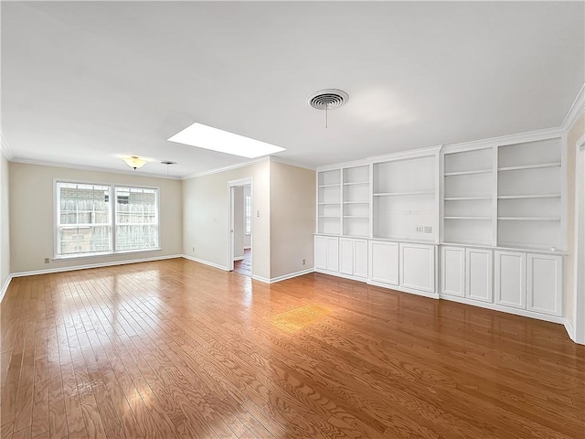 empty room with crown molding, visible vents, a skylight, hardwood / wood-style floors, and baseboards