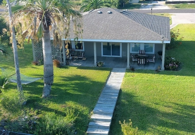 rear view of property featuring roof with shingles, a yard, and a patio