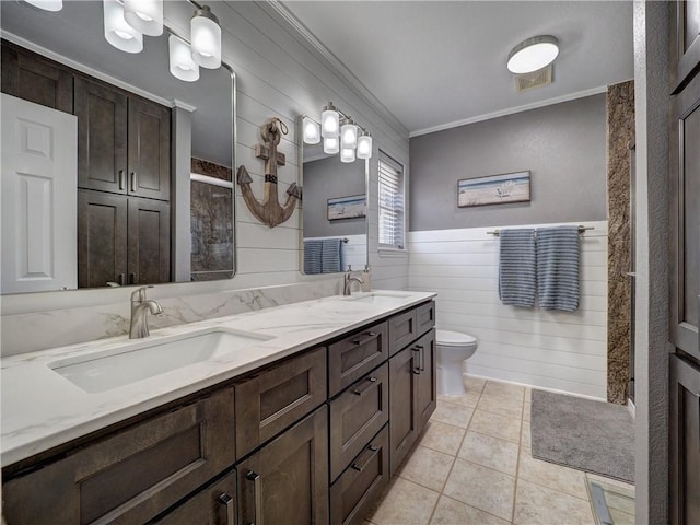 full bathroom with crown molding, toilet, double vanity, a wainscoted wall, and tile patterned flooring