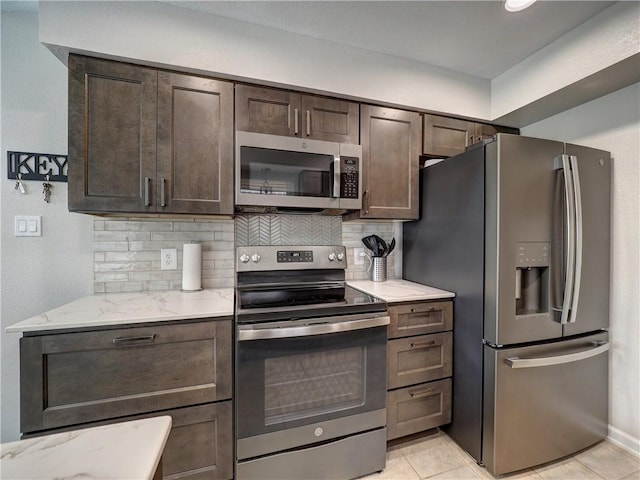 kitchen featuring appliances with stainless steel finishes, dark brown cabinetry, light stone countertops, and tasteful backsplash