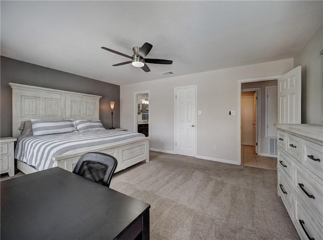 bedroom with baseboards, light colored carpet, a ceiling fan, and ensuite bath