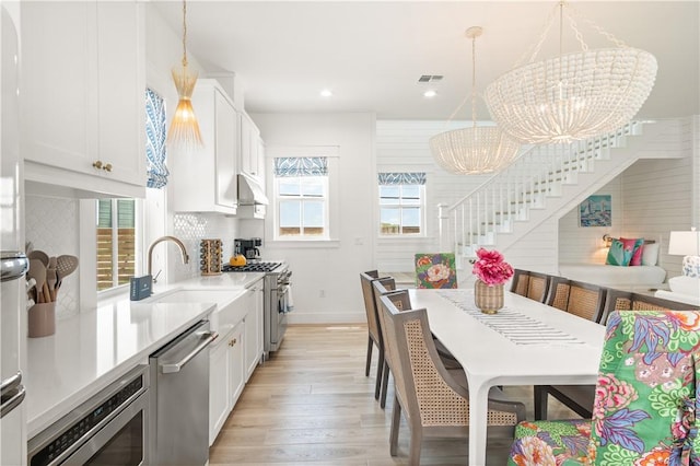 kitchen featuring a sink, a chandelier, appliances with stainless steel finishes, light wood finished floors, and under cabinet range hood
