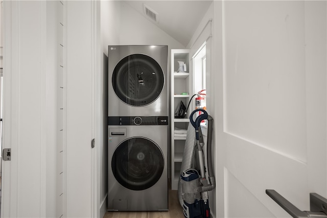 clothes washing area with stacked washer and clothes dryer, wood finished floors, visible vents, and laundry area