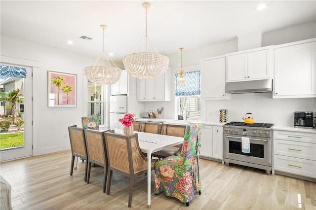 kitchen with under cabinet range hood, high end stove, a notable chandelier, visible vents, and freestanding refrigerator