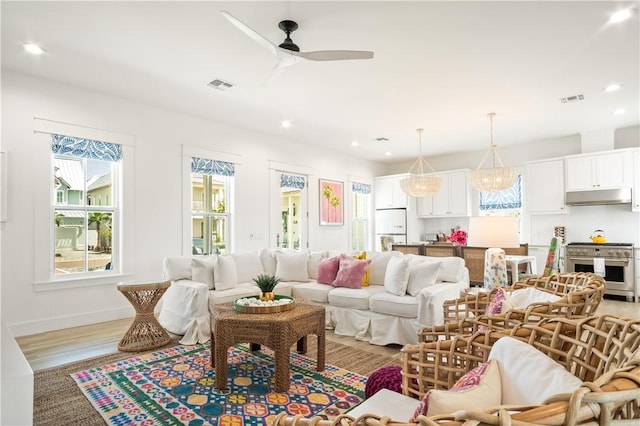 living area featuring light wood-style flooring, a wealth of natural light, a ceiling fan, and visible vents