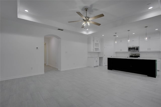 unfurnished living room featuring light hardwood / wood-style floors, ceiling fan, and a raised ceiling