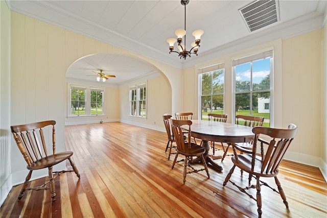 dining room with light wood-type flooring, ceiling fan with notable chandelier, a healthy amount of sunlight, and crown molding