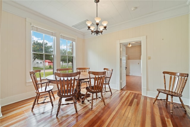 dining room featuring wood walls, hardwood / wood-style flooring, ornamental molding, and a notable chandelier