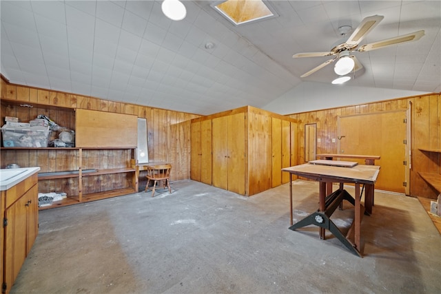 interior space featuring wooden walls, ceiling fan, and vaulted ceiling with skylight