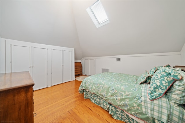 bedroom with vaulted ceiling with skylight, wood-type flooring, and two closets