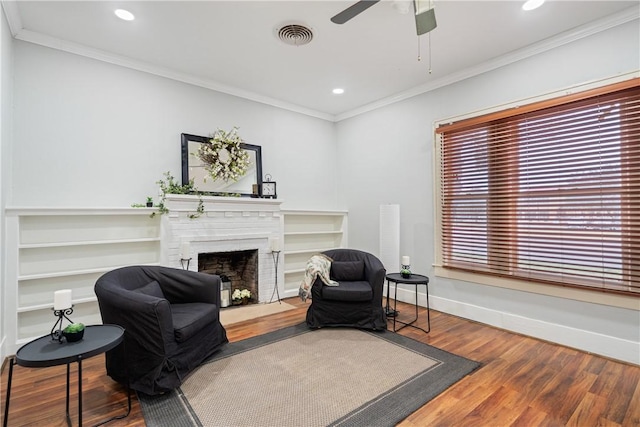 living area featuring a brick fireplace, ceiling fan, hardwood / wood-style flooring, and crown molding