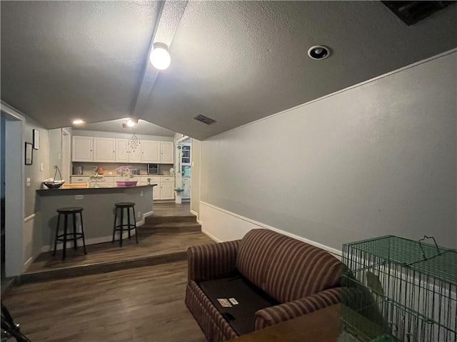 living area featuring dark wood finished floors, lofted ceiling, visible vents, baseboards, and a textured ceiling