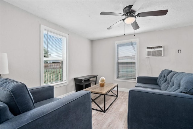 living room with ceiling fan, light hardwood / wood-style flooring, a wall unit AC, and a textured ceiling