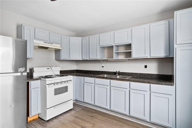 kitchen featuring sink, gas range gas stove, white cabinetry, stainless steel refrigerator, and hardwood / wood-style floors