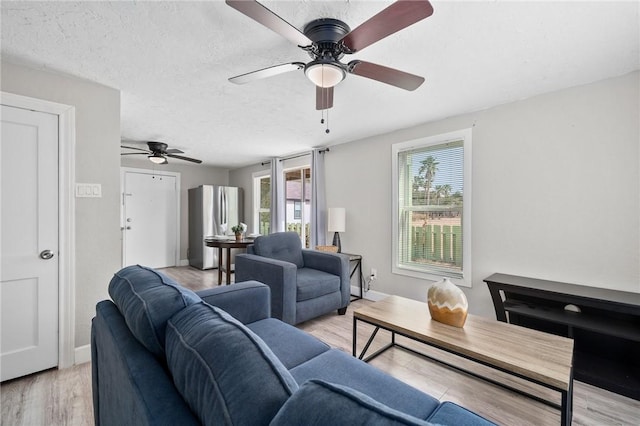 living room with ceiling fan, a textured ceiling, and light wood-type flooring