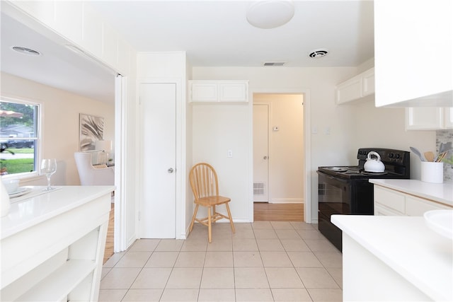 kitchen with white cabinets, light tile patterned floors, and black / electric stove