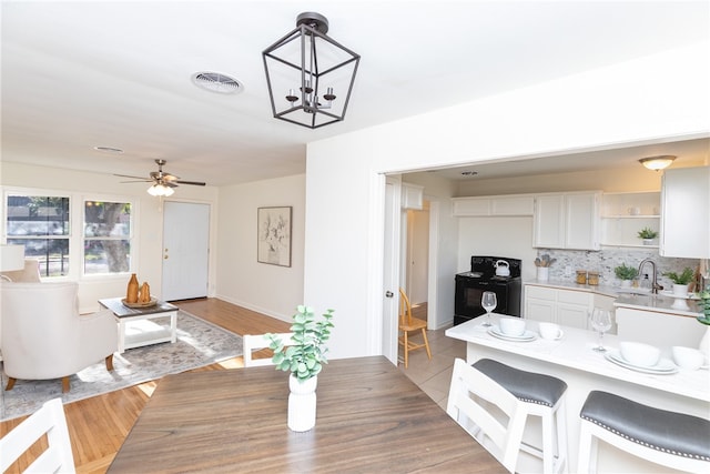 dining room with sink, ceiling fan with notable chandelier, and light wood-type flooring