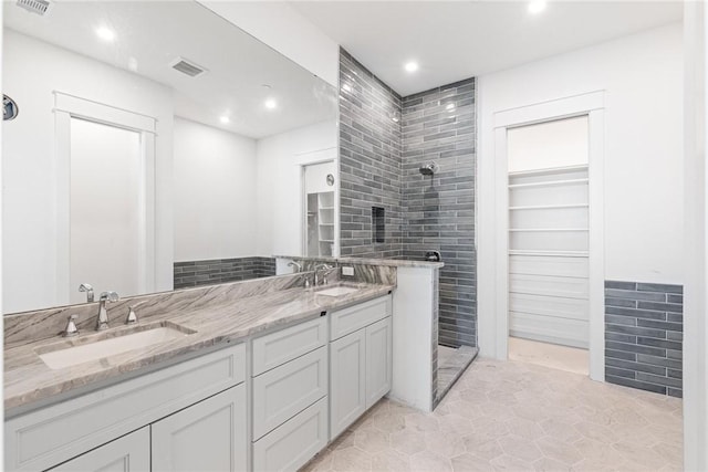 bathroom featuring double vanity, visible vents, a walk in shower, and a sink