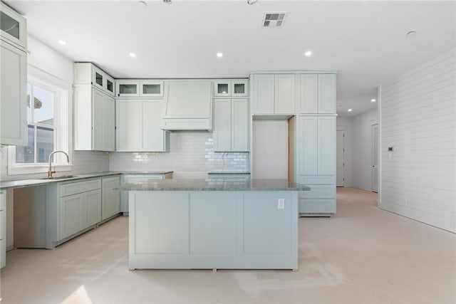 kitchen with wall chimney range hood, tasteful backsplash, a sink, and visible vents