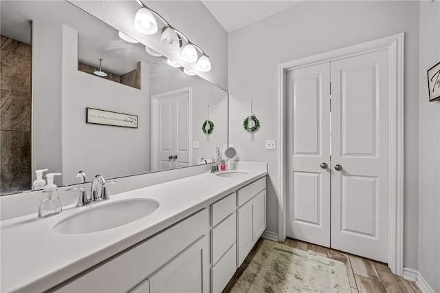 full bathroom with a sink, baseboards, double vanity, and wood finished floors